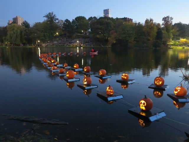 Halloween pumpkin lanterns floating on Central Park lake at dusk.