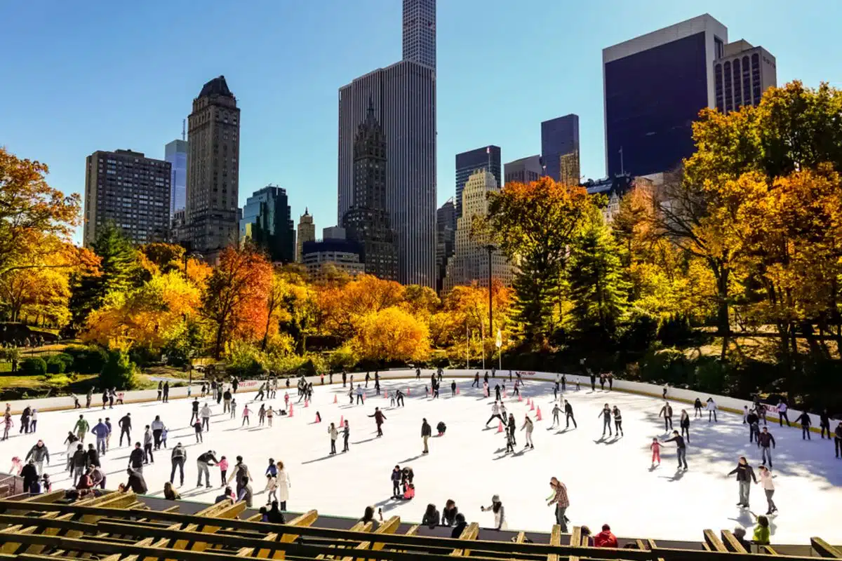 Central park ice skating rink in autumn with city skyline in background.